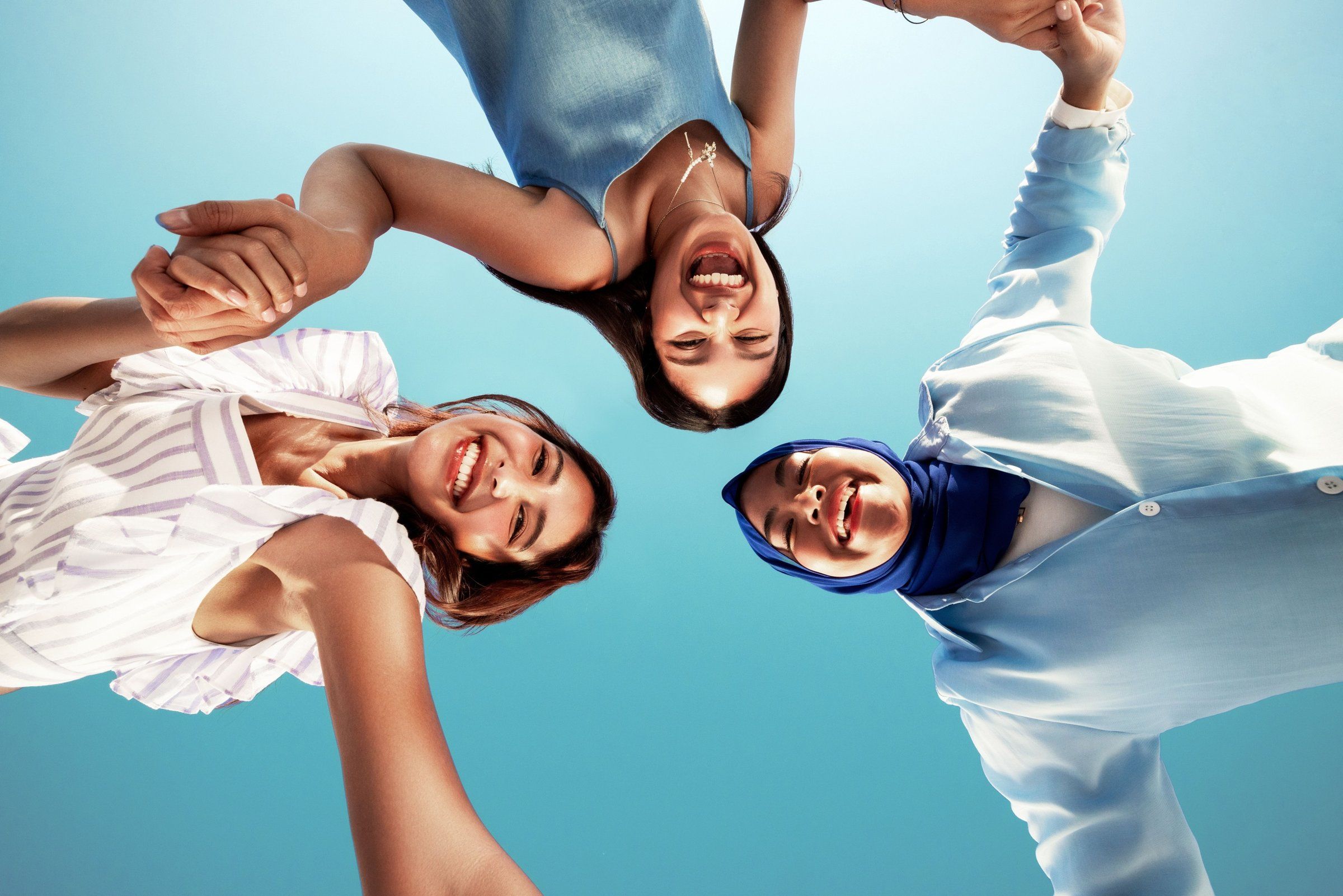 Three friends laughing together under a blue sky