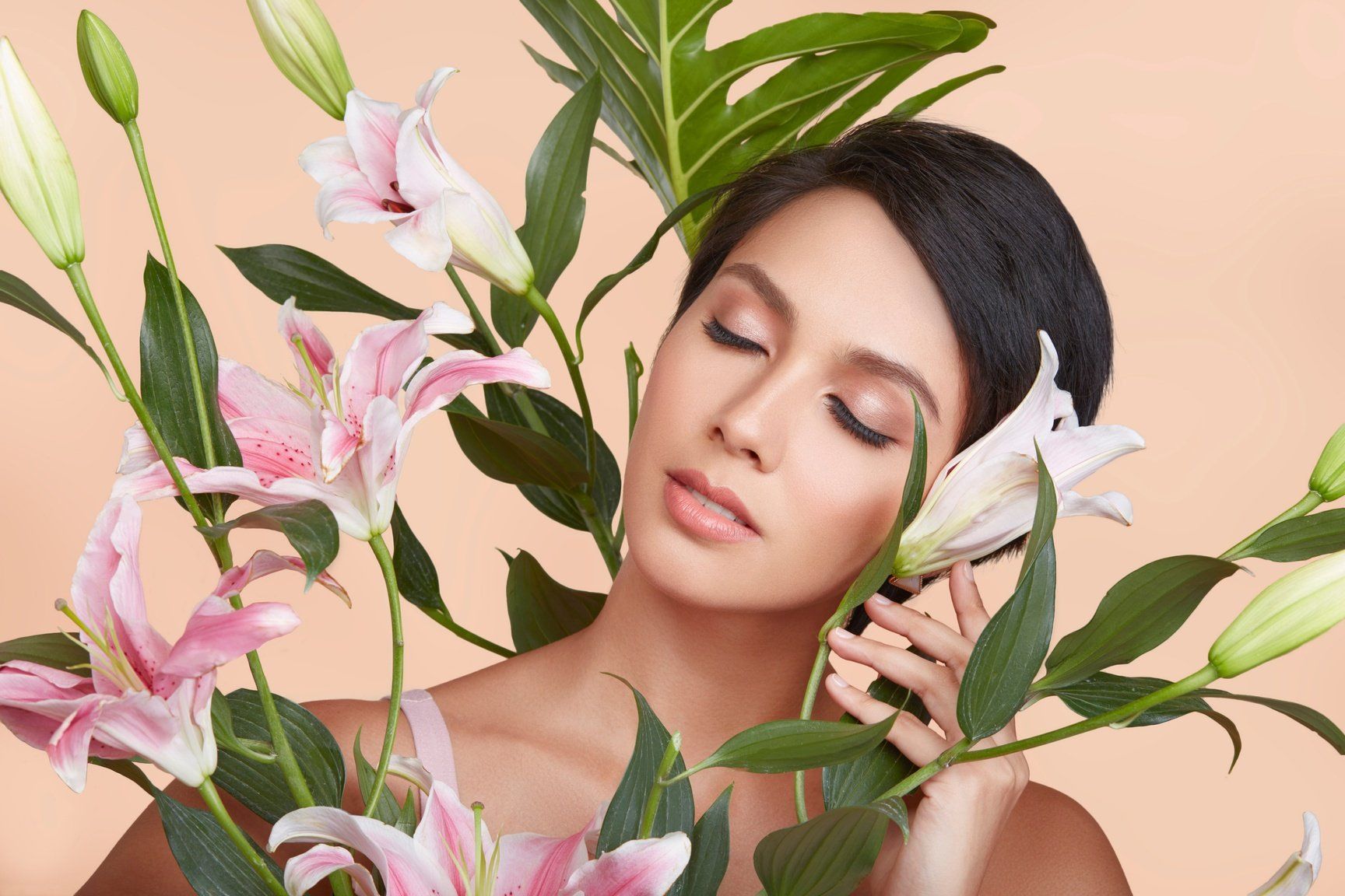Model with eyes closed surrounded by pink lilies